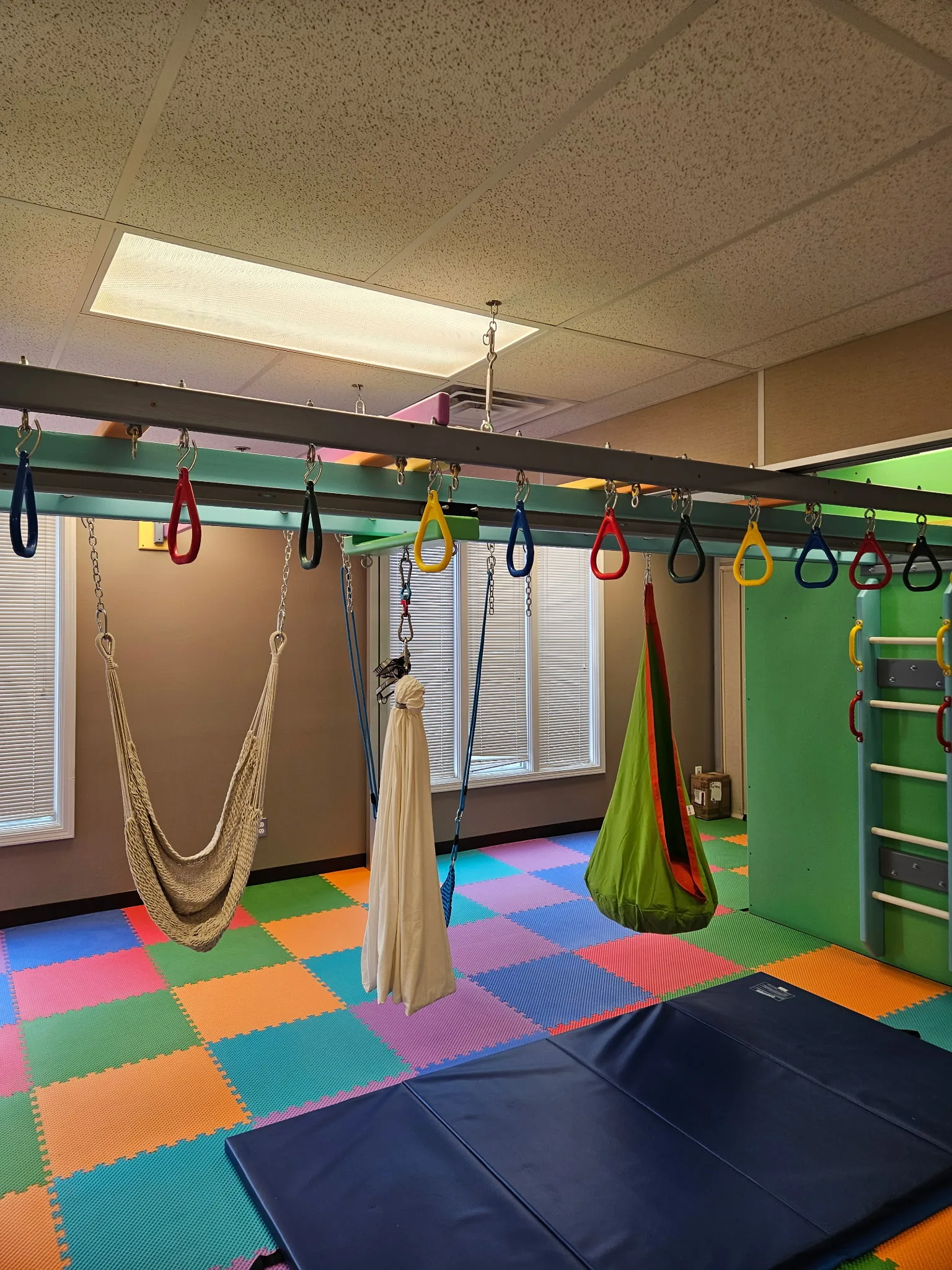 Rope hammock, lycra swing, and green cocoon swing hanging from an overhead ring track above a crash mat