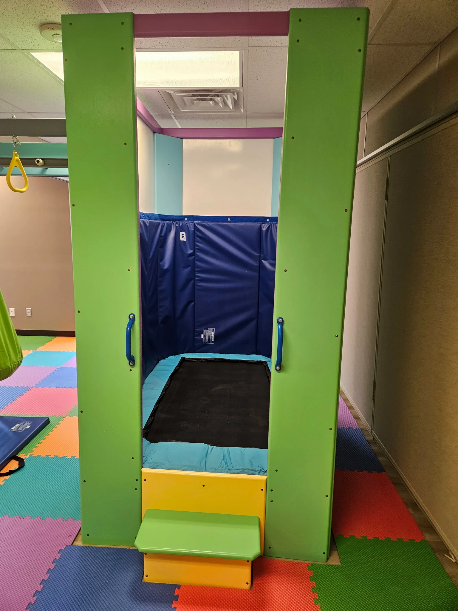 Enclosed padded nook with a small in-ground trampoline framed by green panels and a yellow step