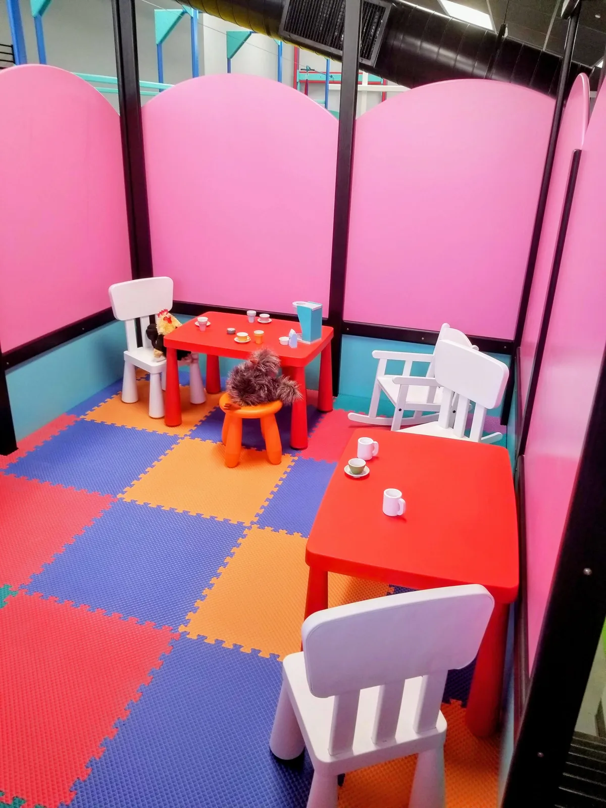 Child-sized table and chairs in a pink corner beside colorful floor mats