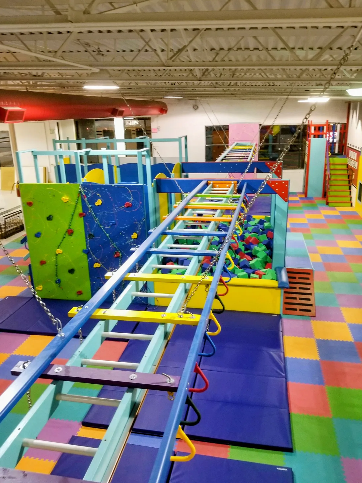 Elevated view along an overhead ladder above colorful padded flooring and climbing equipment