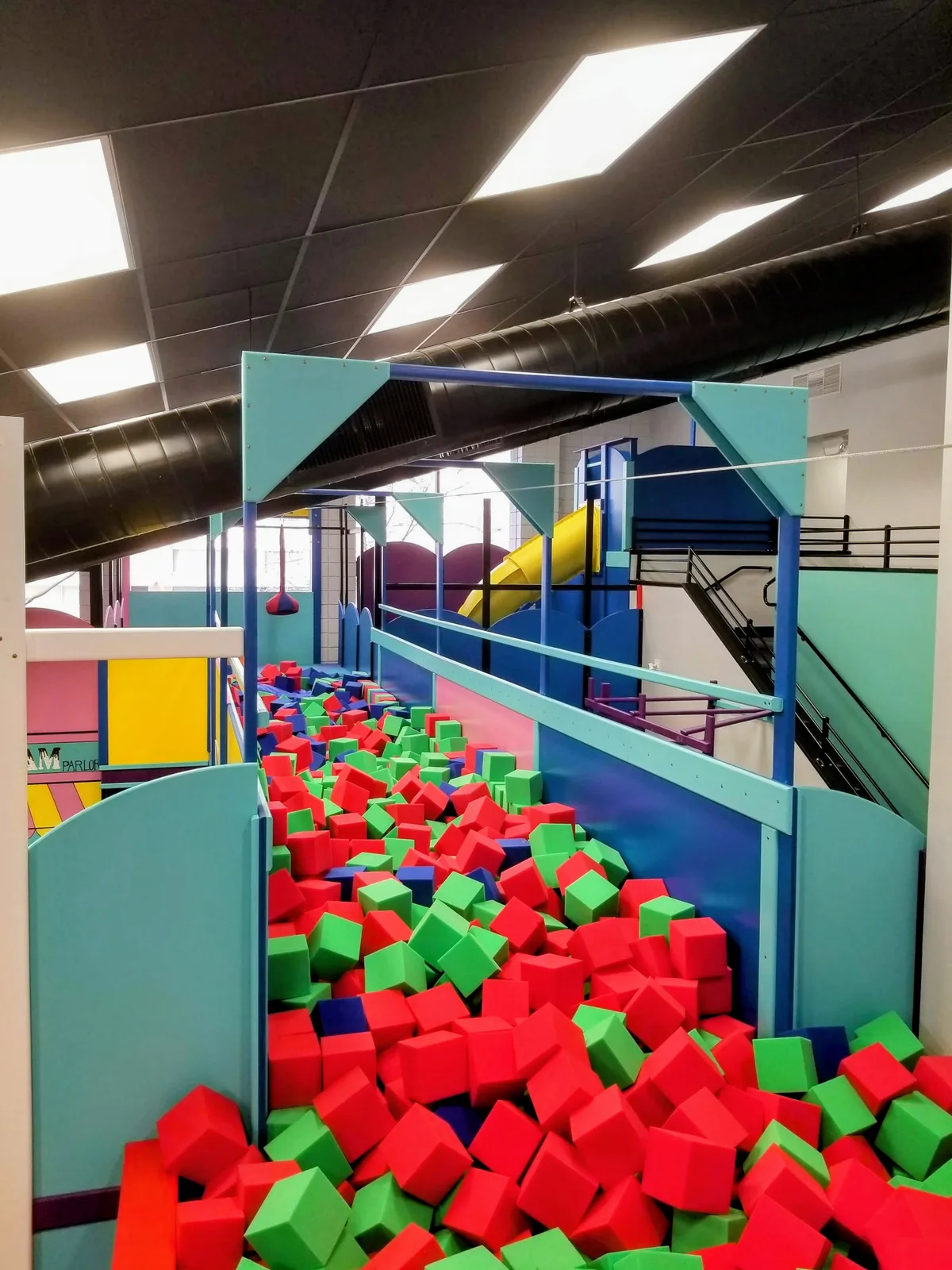 Large pit filled with red and green foam blocks beside a climbing structure