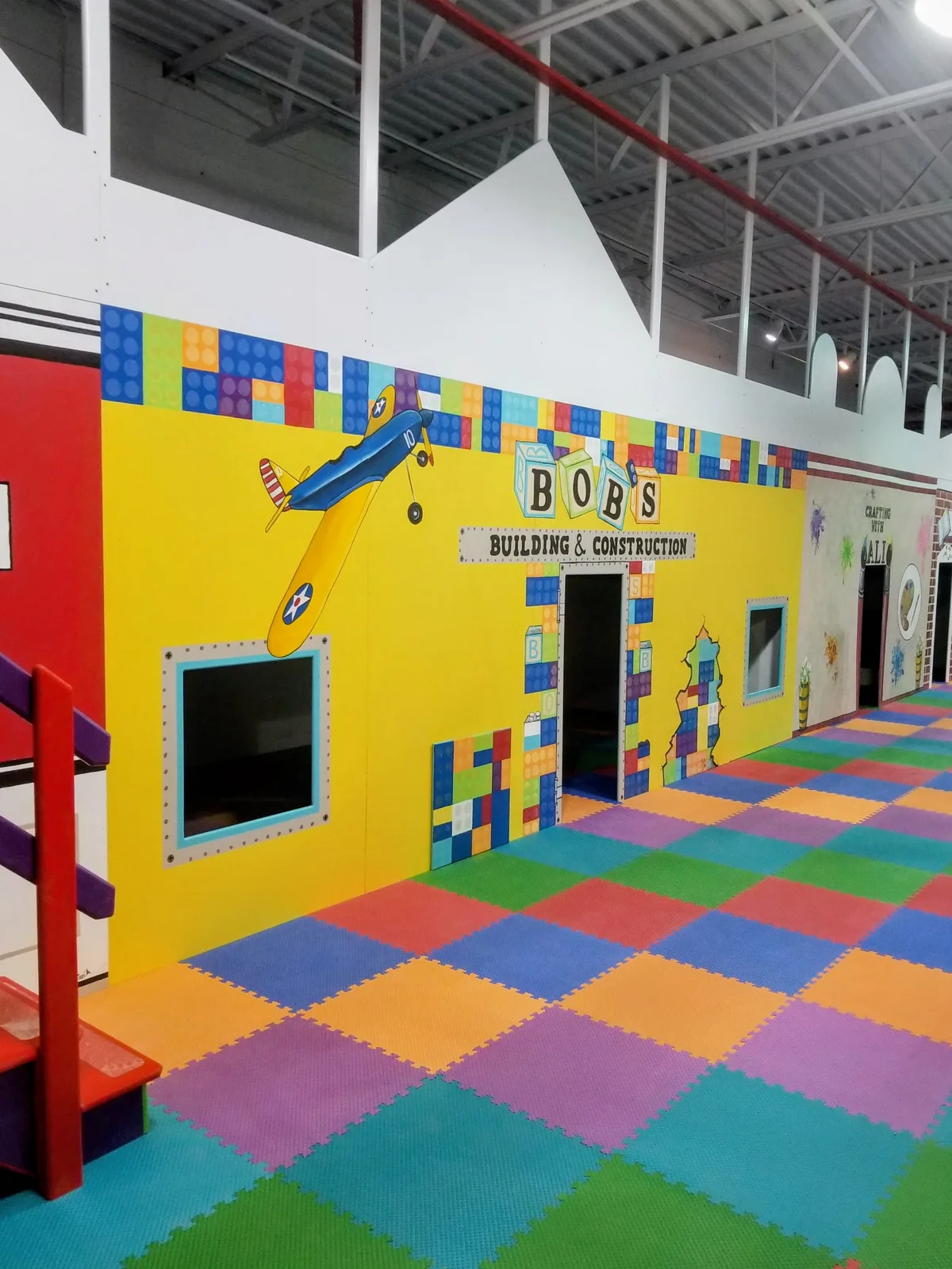 Sensory gym with a colorful building-block mural, padded flooring, and climbing equipment