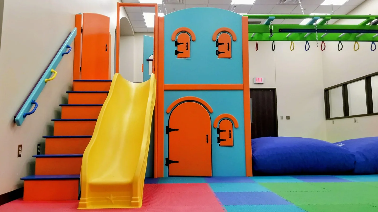 Yellow slide beside an orange and teal playhouse structure with blue landing pads