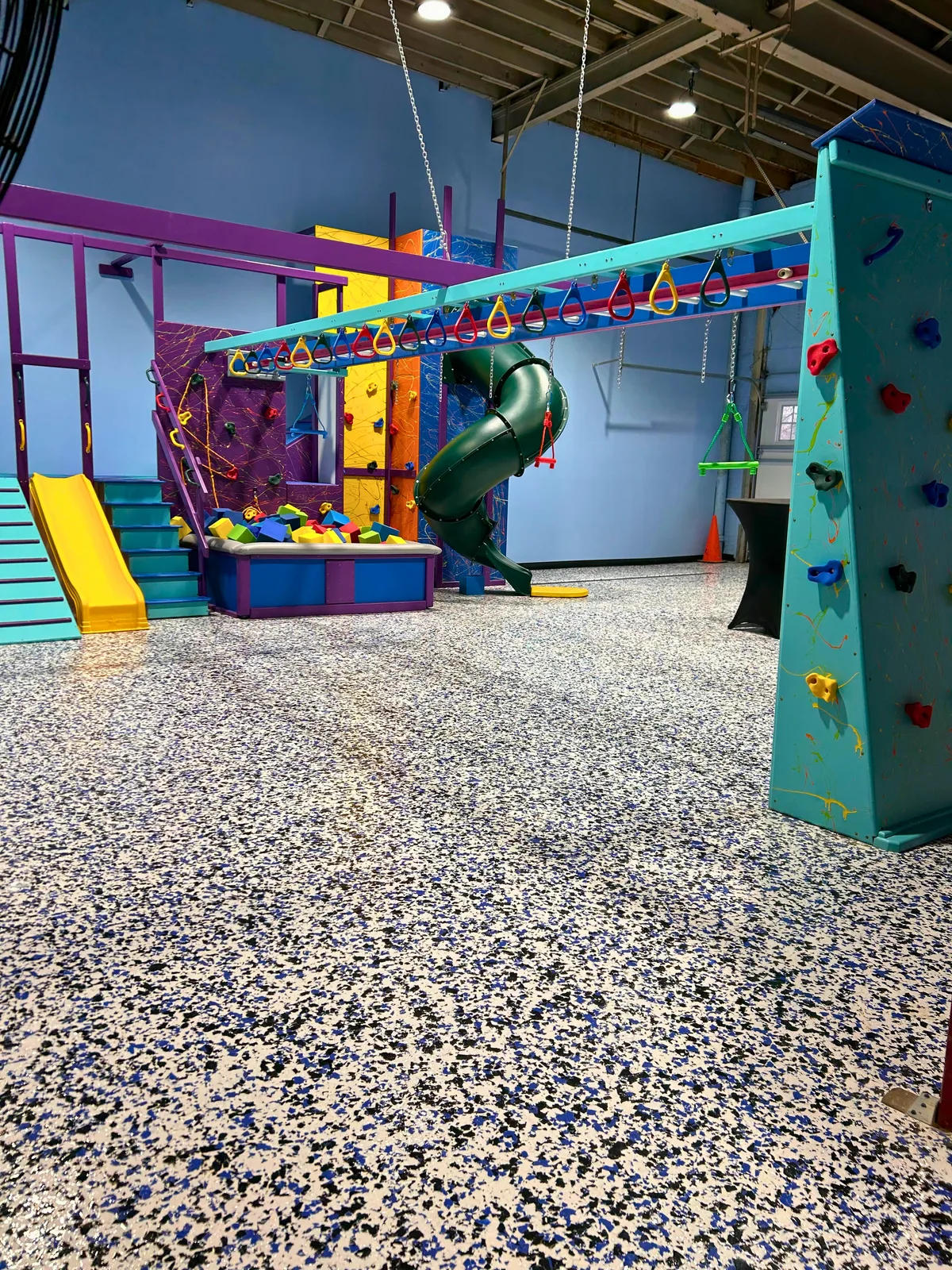 Low view of an overhead swing frame and colorful climbing panels in a carpeted gym