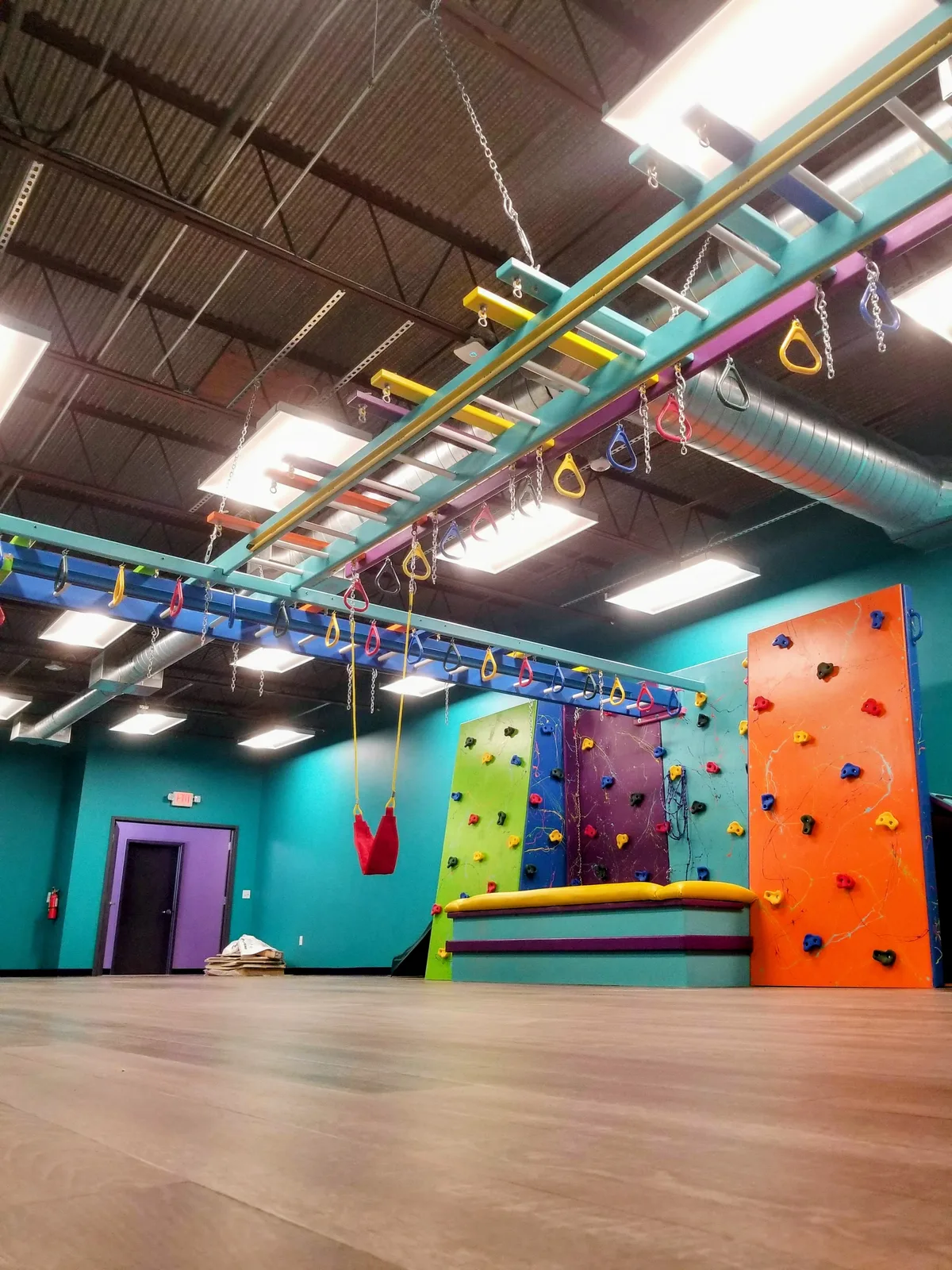 Sensory gym with teal, orange, and purple climbing walls beneath a colorful overhead frame