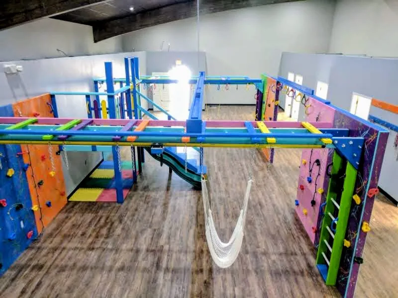 Elevated view of a sensory gym with colorful overhead bars, climbing panels, a ramp, and a white hammock