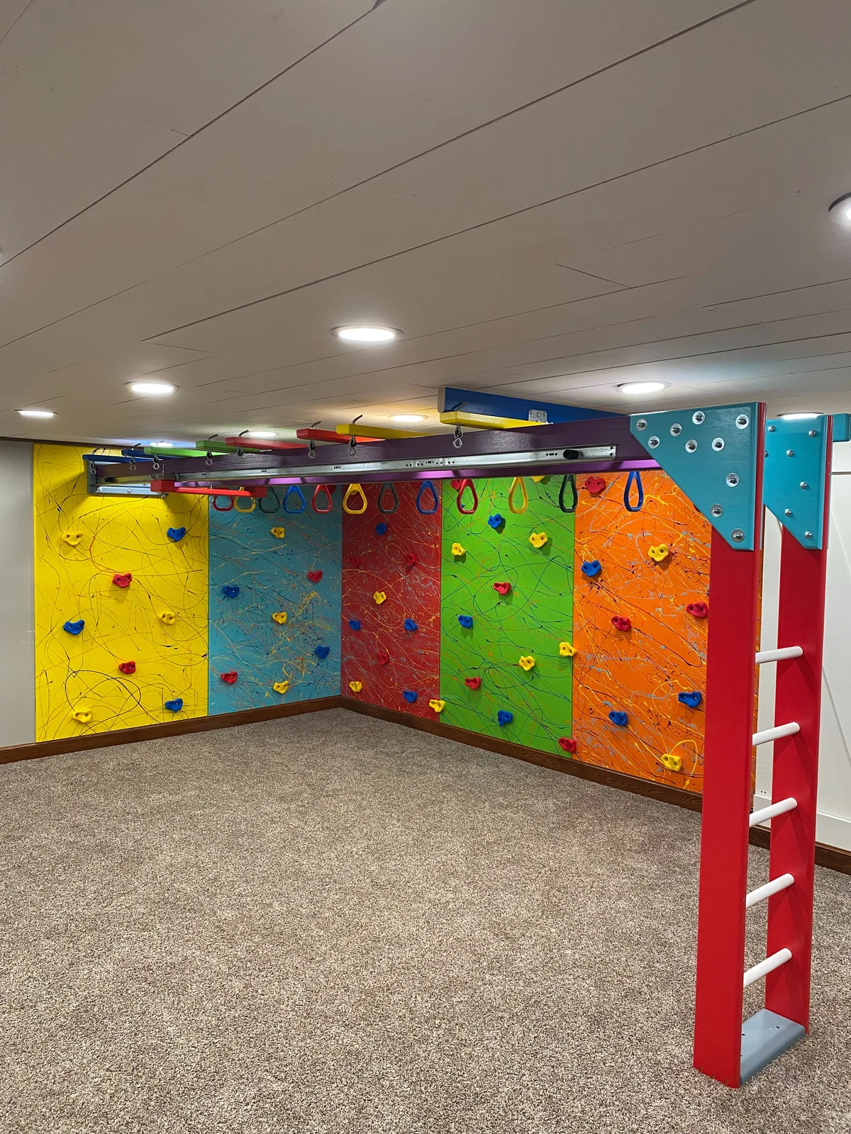 Carpeted residential room with colorful climbing walls fitted along two sides
