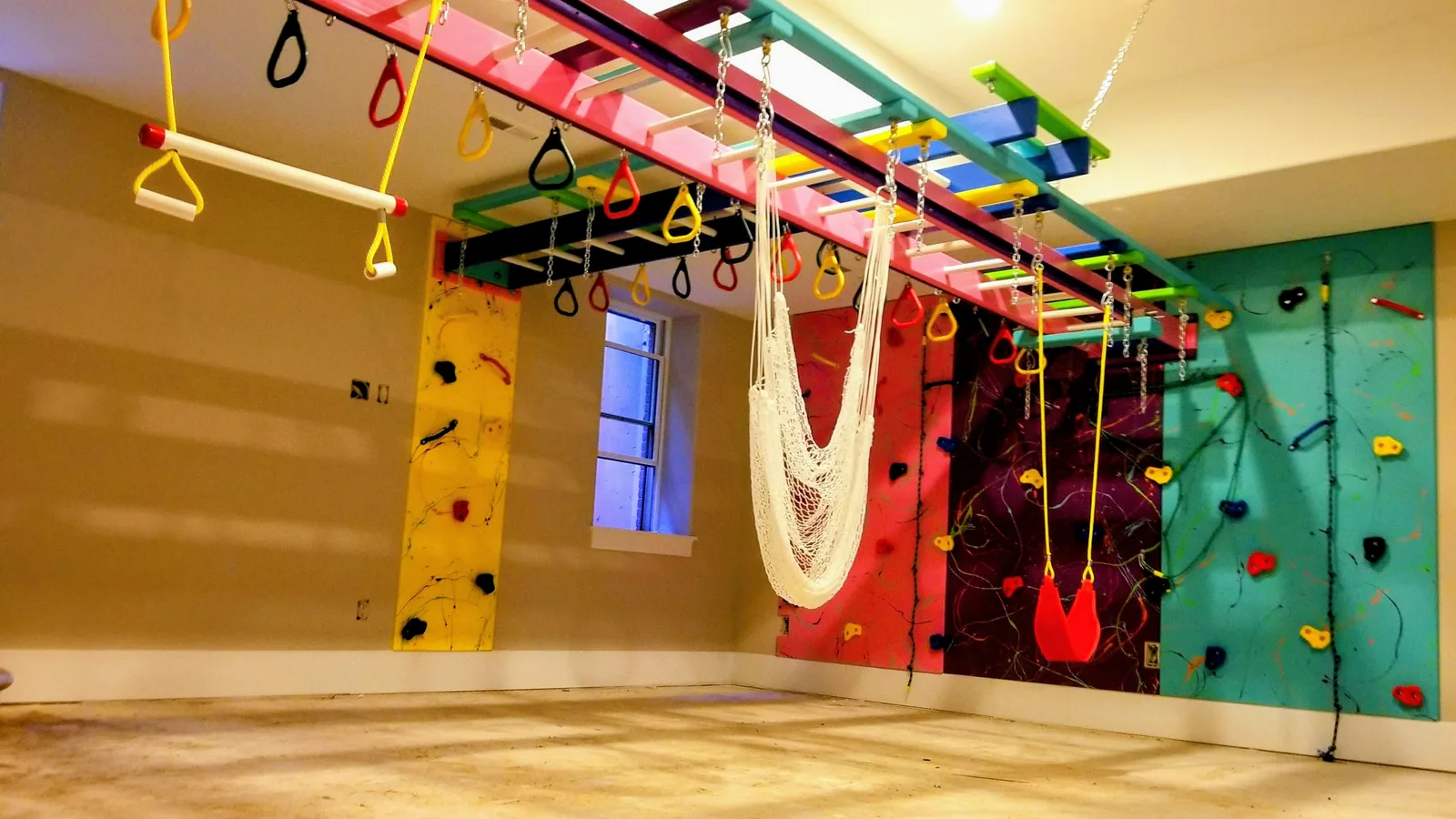 Residential gym with colorful climbing walls, overhead bars, hanging rings, and a white hammock
