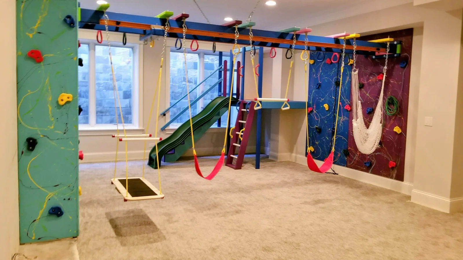 Carpeted home gym with climbing walls, red swings, a small platform swing, and a white hammock
