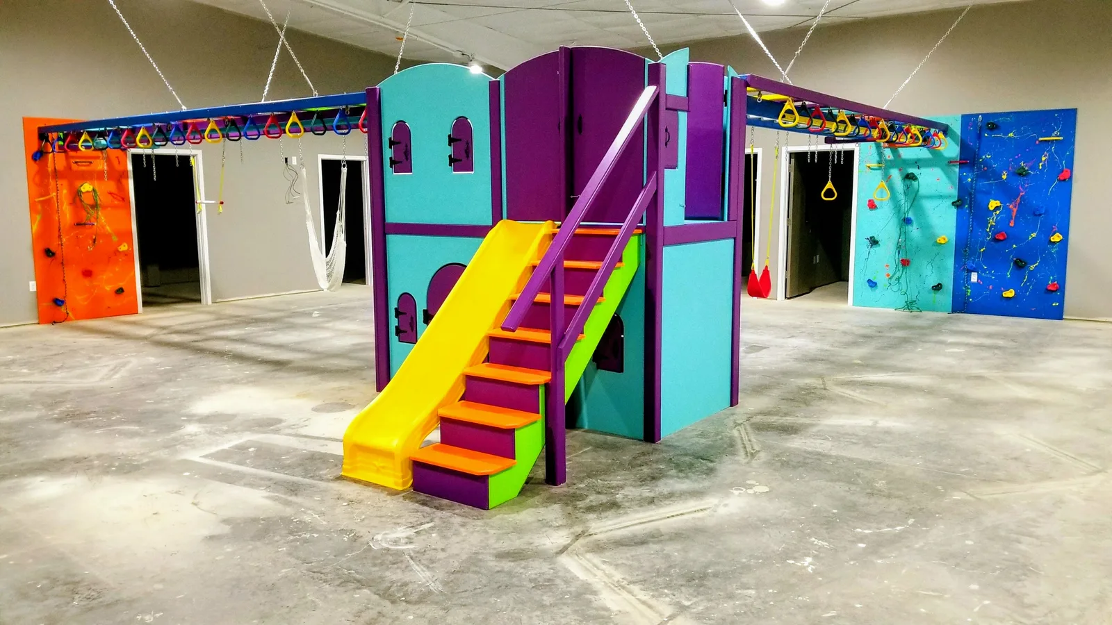 Teal and purple castle structure with yellow steps beside colorful climbing walls
