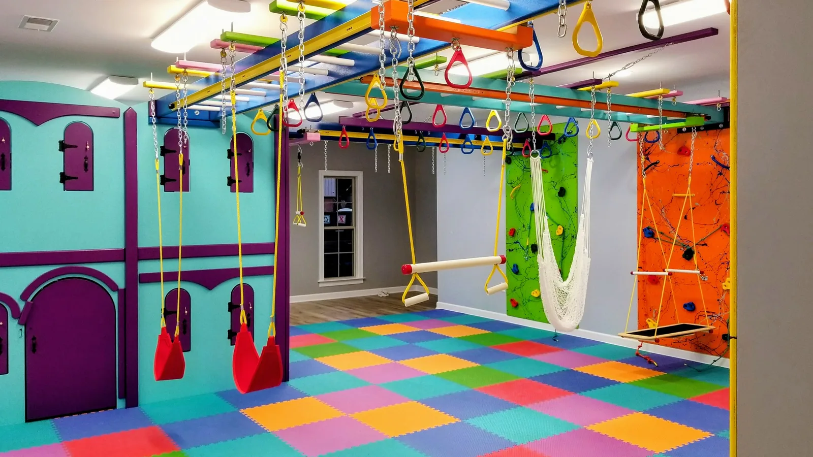 Colorful home sensory gym with hanging rings, fabric swings, a climbing frame, and padded flooring