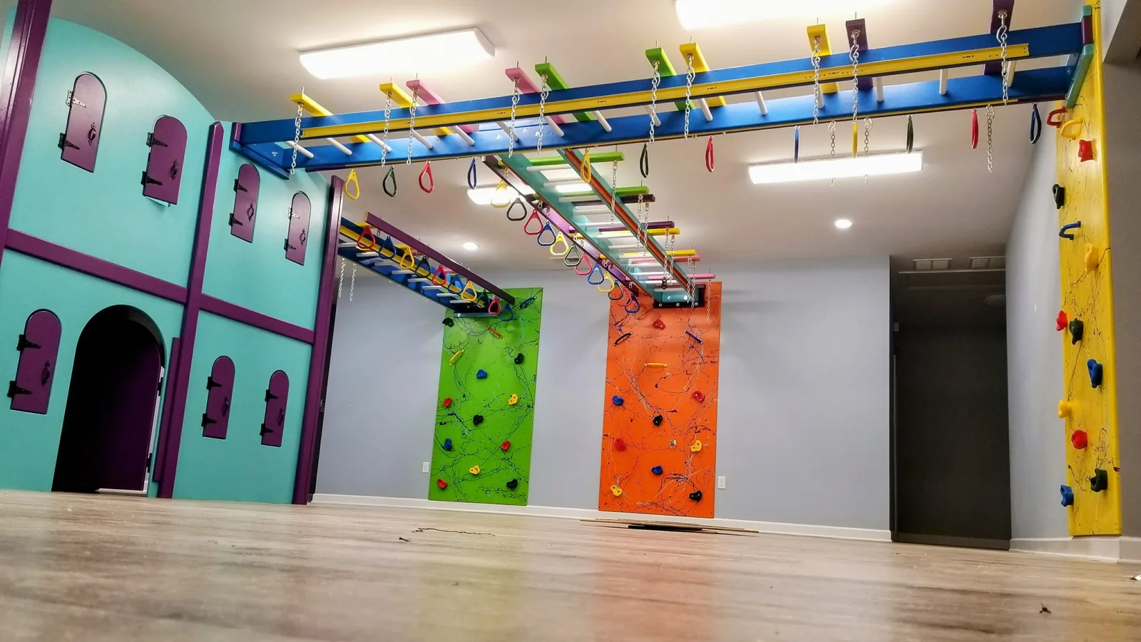 Residential sensory gym with teal and purple castle panels, colorful climbing walls, and overhead bars