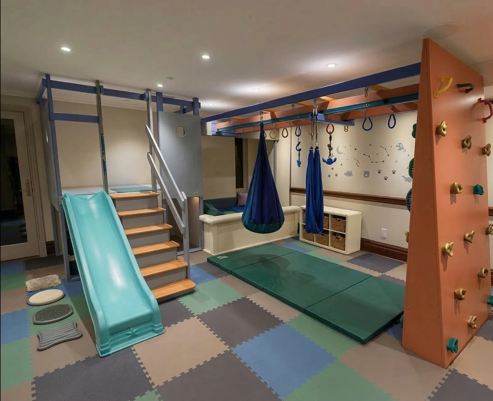 Home sensory gym with a teal slide, padded steps, climbing panels, and a suspended fabric swing